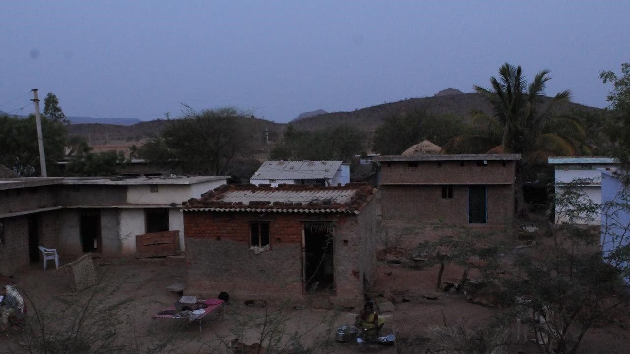 A group of people sitting on the ground in front of some buildings.