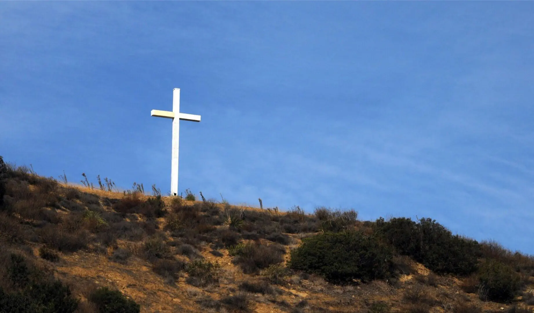 A cross on top of a hill with trees in the background.