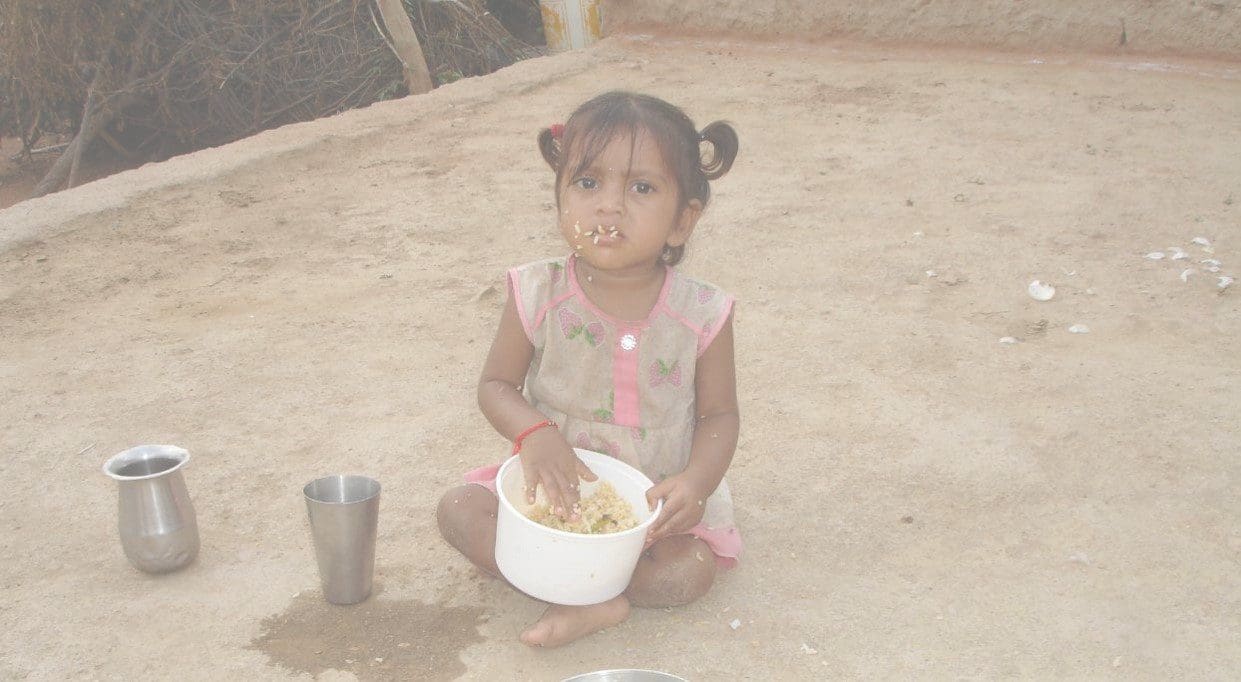 A little girl sitting on the ground with food in her hands.