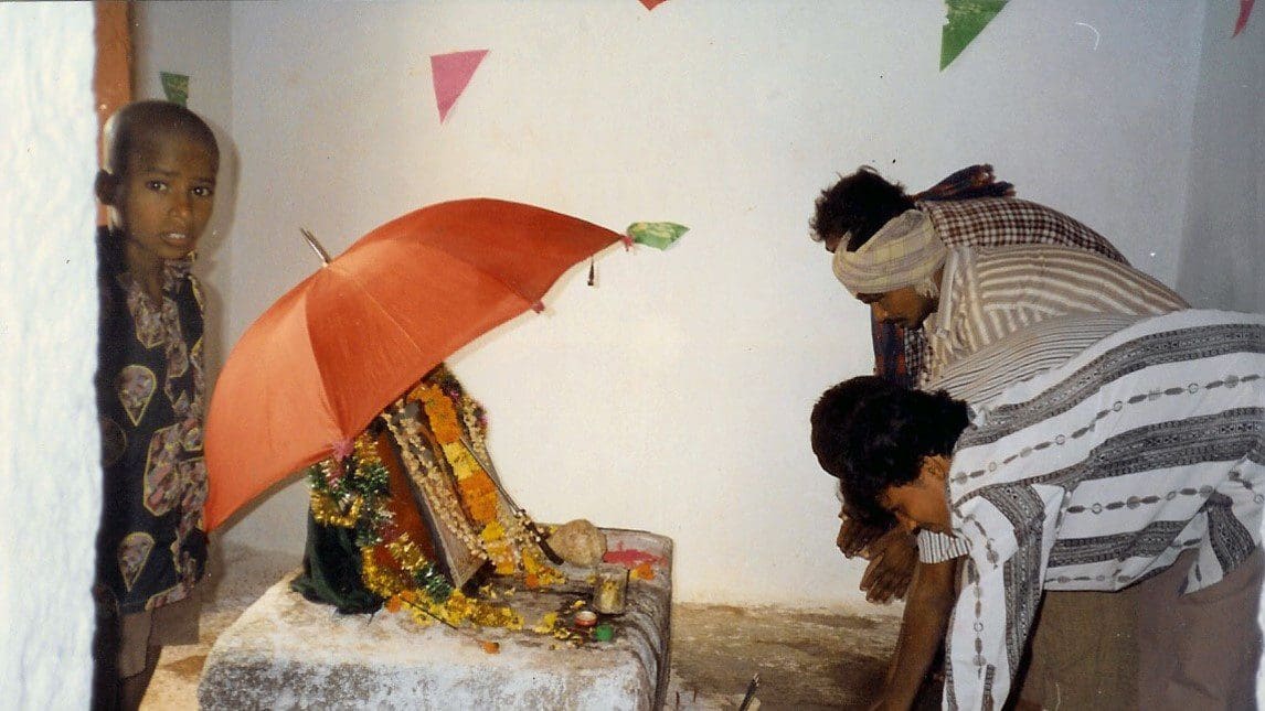 A woman sitting on top of a bed under an umbrella.