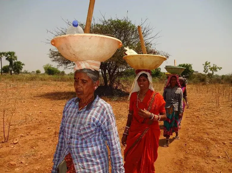 A group of people walking in the dirt with baskets on their heads.