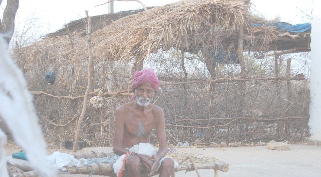 A man sitting on the ground in front of a hut.