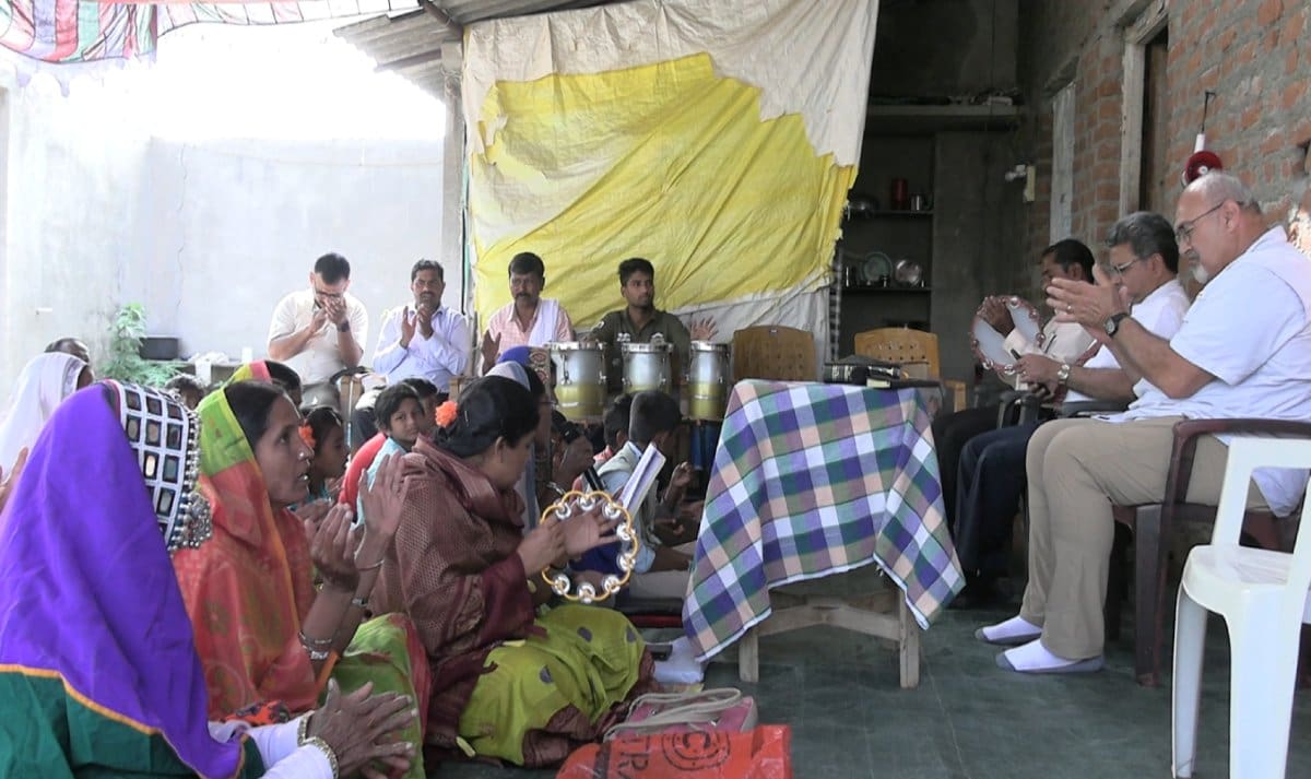 A group of people sitting around in front of a yellow and white tent.