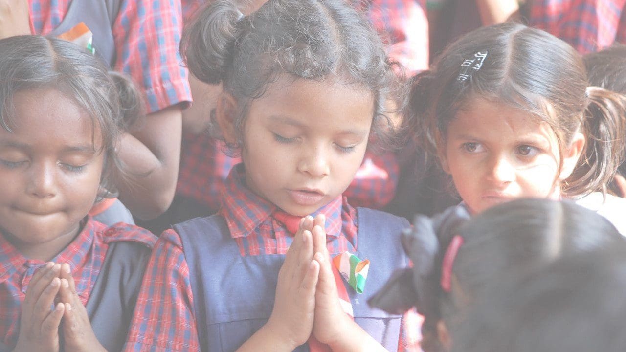 A little girl is praying in front of some other children.