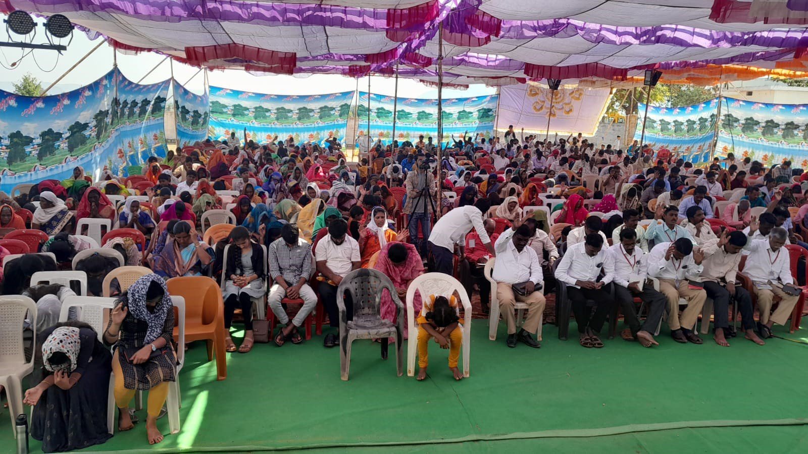 A large group of people sitting in chairs under an awning.