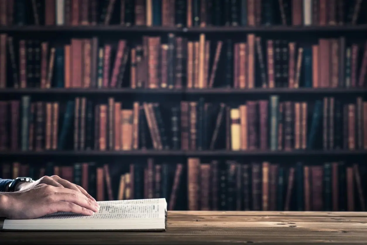 A person is reading a book in front of bookshelves.