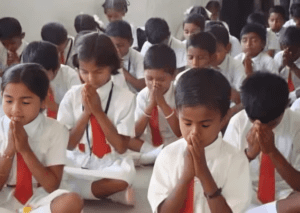 A group of children sitting in the floor praying.