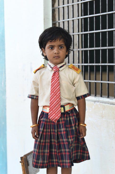 A young boy in school uniform standing outside.