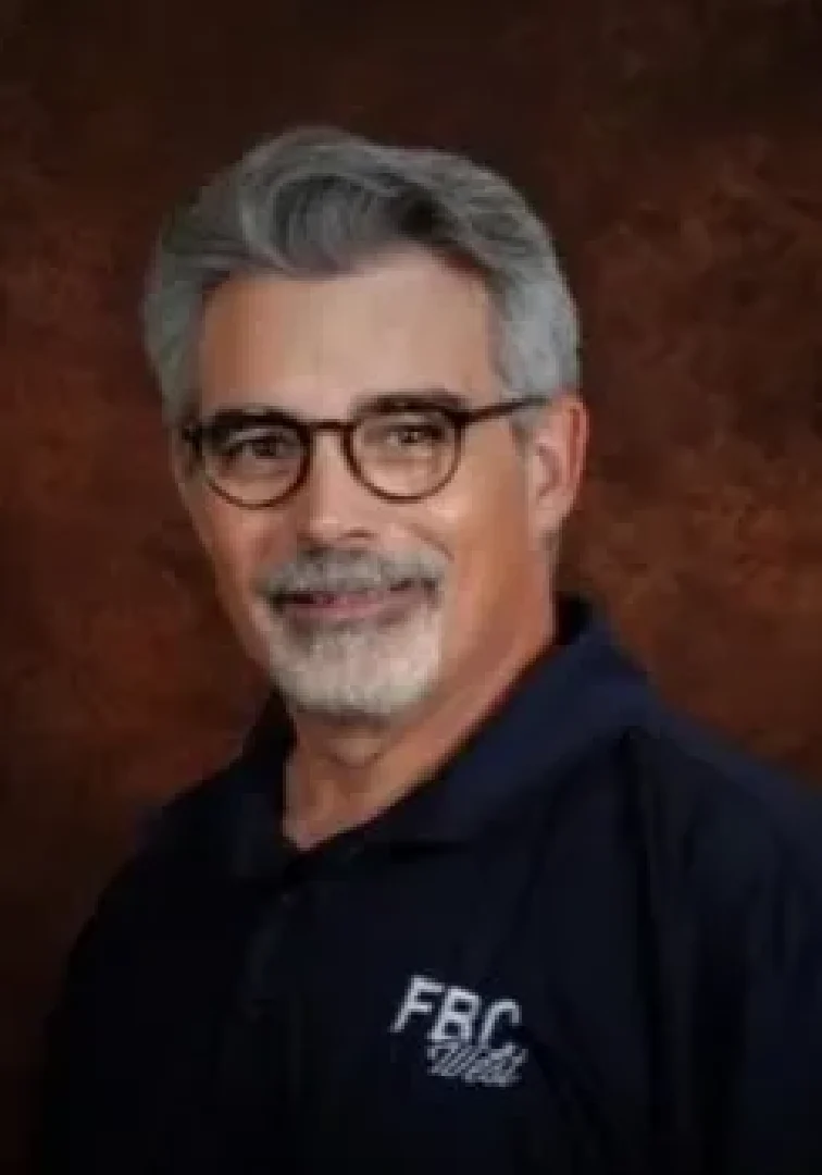 A man with grey hair and glasses is smiling.