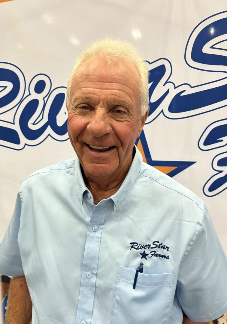 A man with white hair and blue shirt smiling.