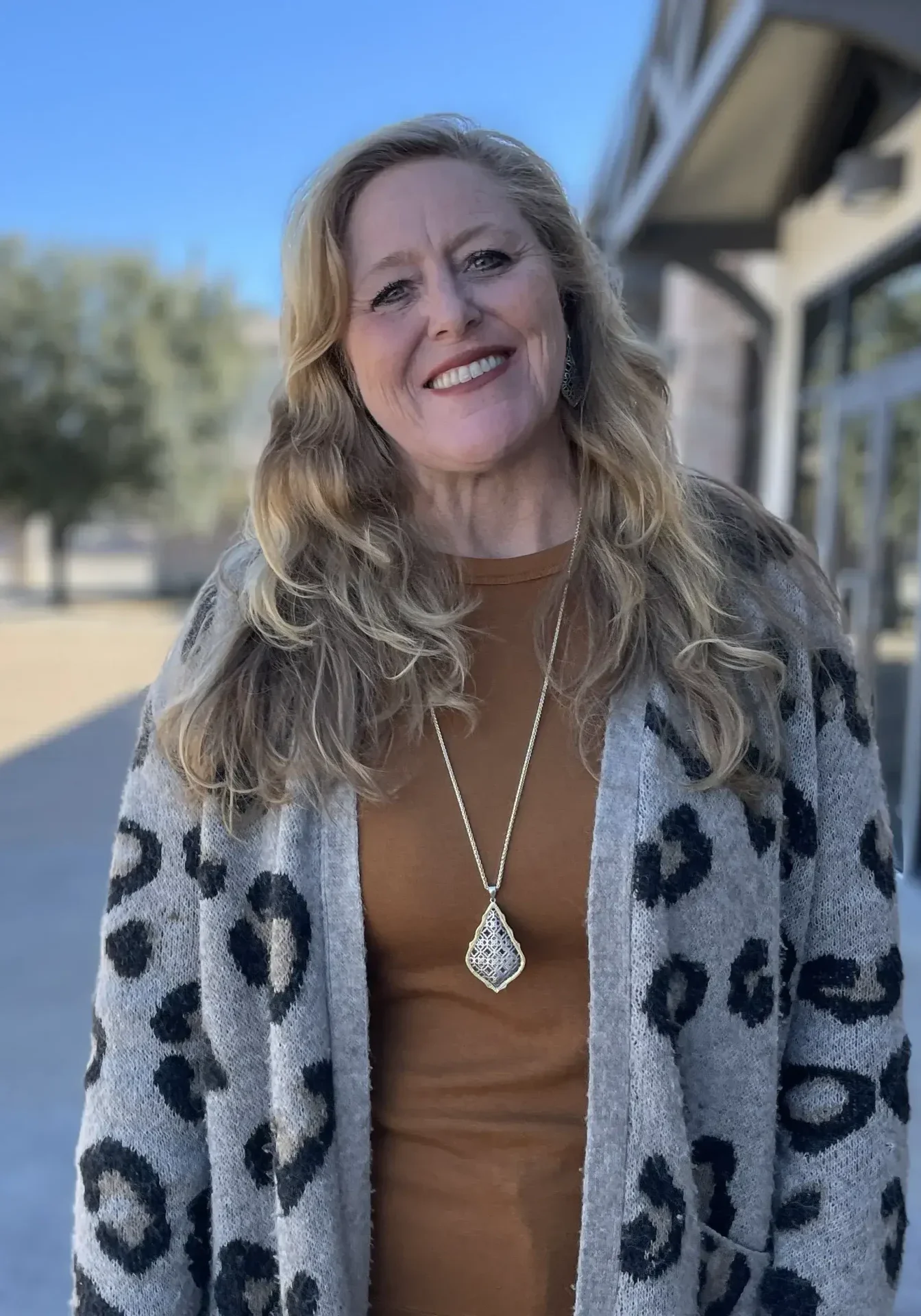 A woman standing on the sidewalk wearing a brown top and leopard print coat.