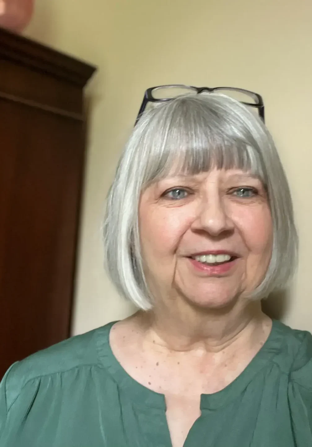 A woman with short hair and glasses is smiling.